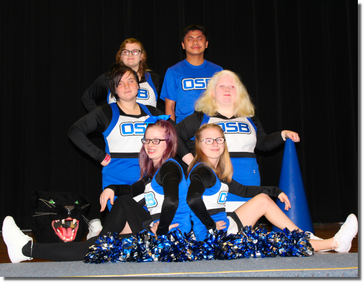 Six Cheerleaders posing with two sitting on the floor, two kneeling, and two standing